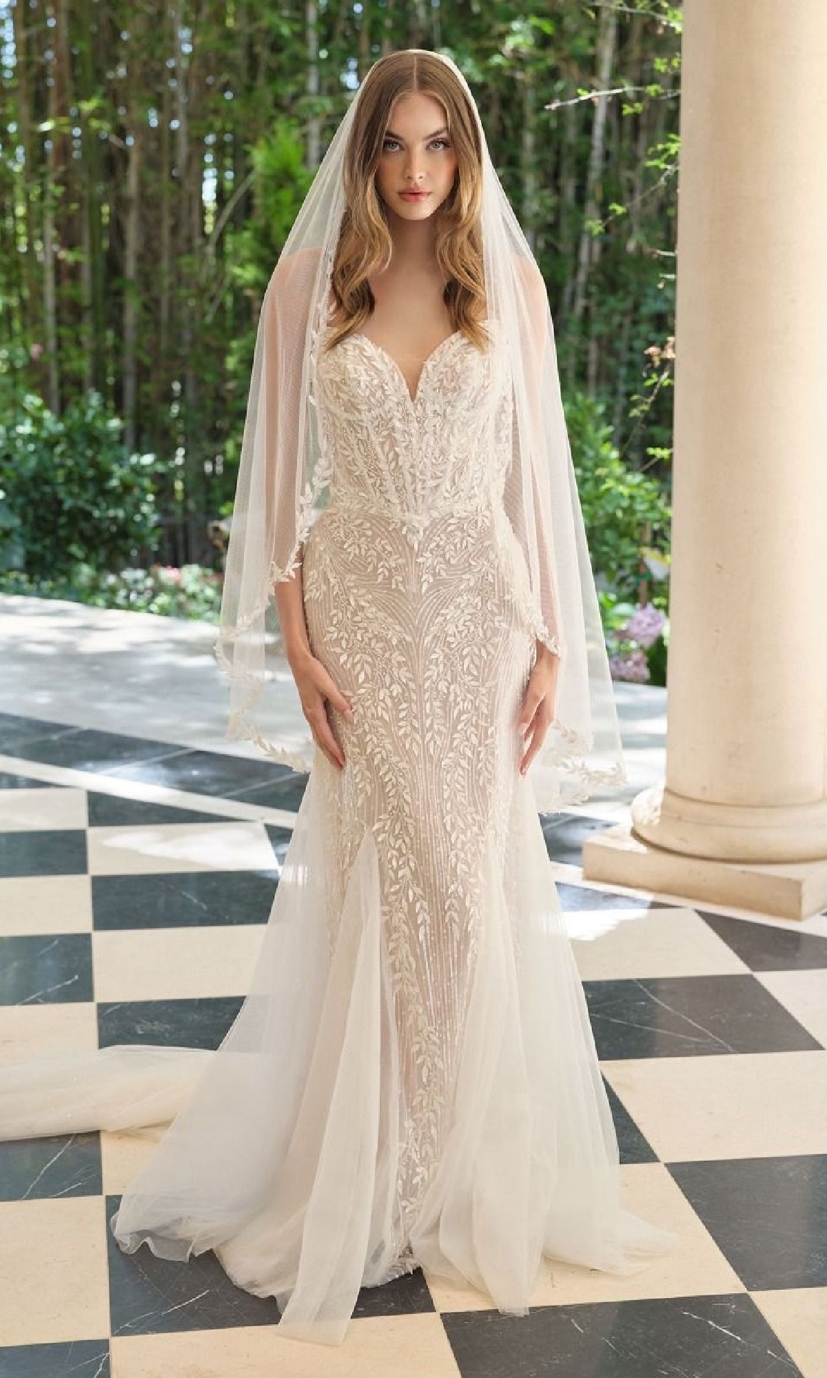 Woman wearing a white lace wedding dress with a veil in an outdoor setting.